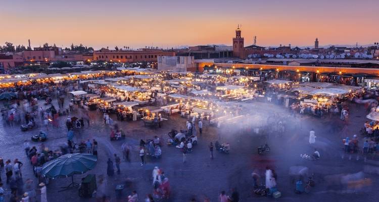 Belebter Marktplatz mit Menschen und Ständen in der Dämmerung.