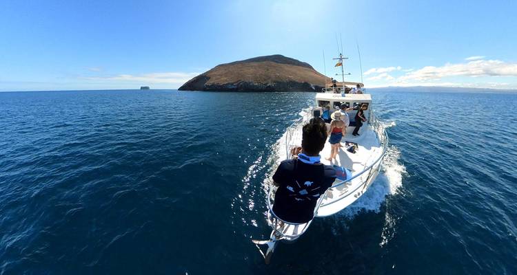 Petit bateau d'excursion filant à travers l'océan bleu profond vers une île rocheuse des Galápagos sous un ciel dégagé.