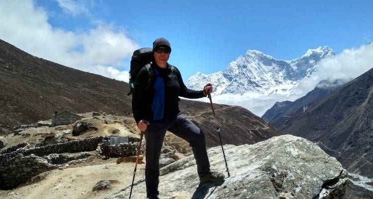 Hiker with trekking poles standing on a rocky outcrop with mountains in the background.