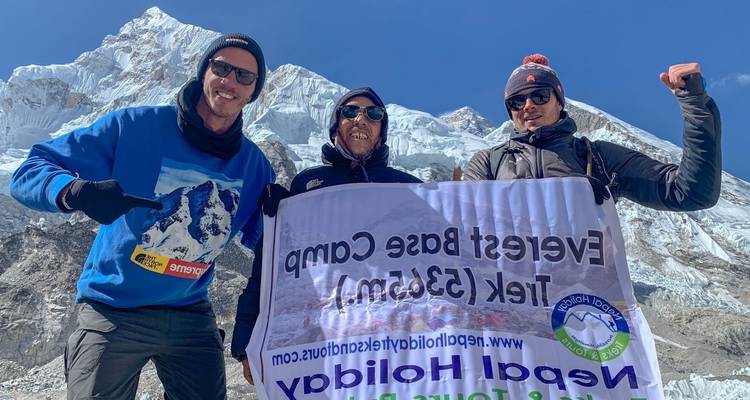 Three people posing with a sign at Everest Base Camp.