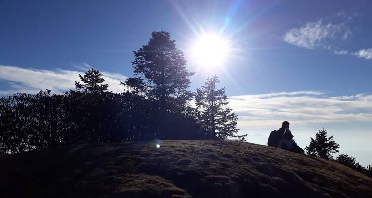 Silhouetted figure sitting on a hill at sunset.