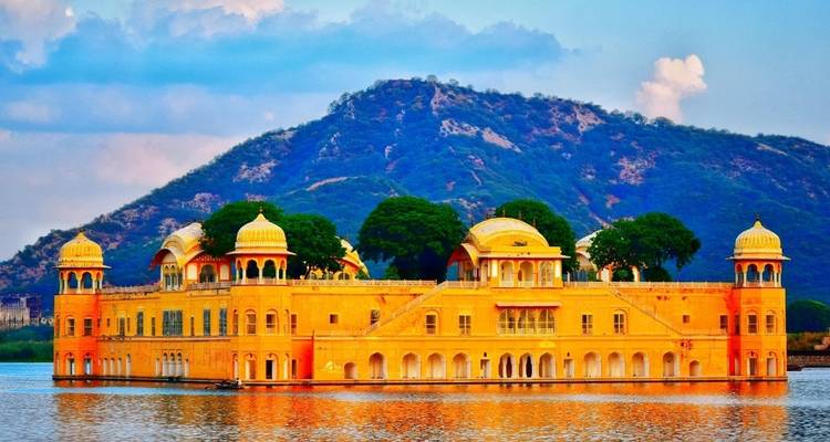 Jal Mahal palace in the middle of a lake with hills behind.
