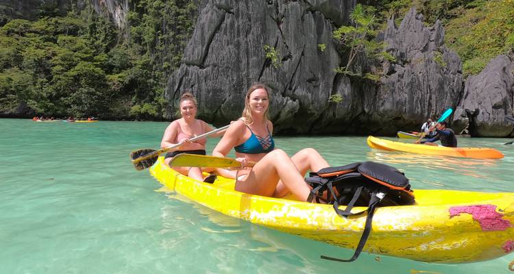 Deux femmes faisant du kayak sur une eau turquoise près de falaises calcaires.
