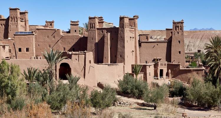 Aït Benhaddou, un village fortifié historique constitué de bâtiments en terre cuite entouré de désert et de végétation.