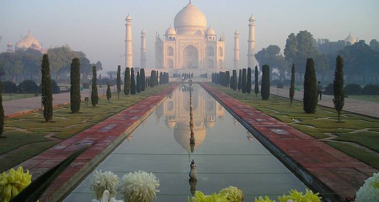 View of the Taj Mahal with reflection in a pool and people walking.