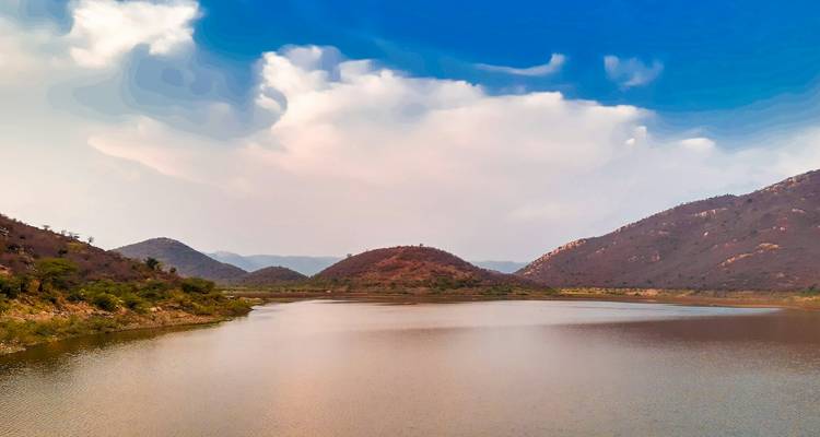 Scenic view of a lake surrounded by hills under a blue sky.