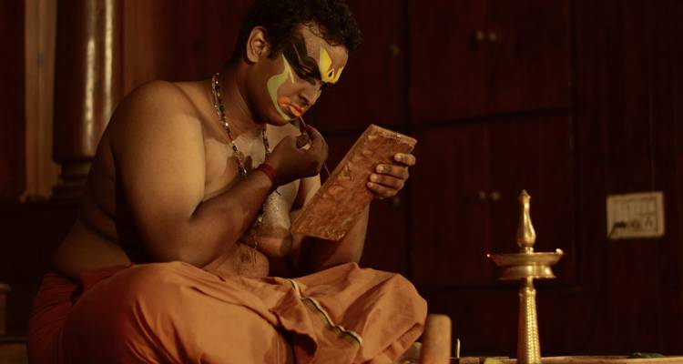 Kathakali-artiest in Kerala die zorgvuldig kleurrijke gezichtsmake-up aanbrengt onder warm podiumlicht.