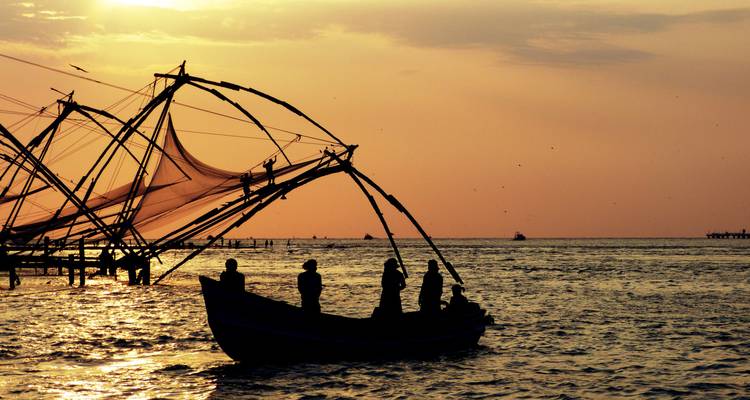 Gesilhouetteerde vissers in een boot naast Chinese visnetten bij gouden zonsondergang boven de Arabische Zee.