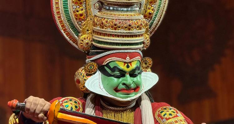 Uitbundig gekostumeerde Kathakali-danser met levendige groene gezichtsverf die optreedt op het podium.