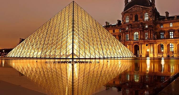Louvre glass pyramid glowing warmly at dusk with perfect reflection in the still water pool.