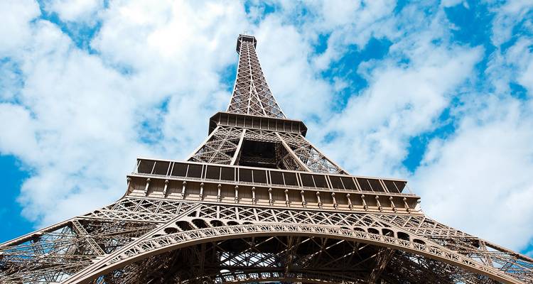 Dramatic low-angle shot of the Eiffel Tower against a bright blue sky dotted with clouds