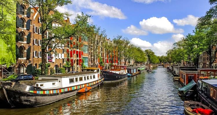 Colourful canal houses and moored boats line a sunny waterway in Amsterdam.