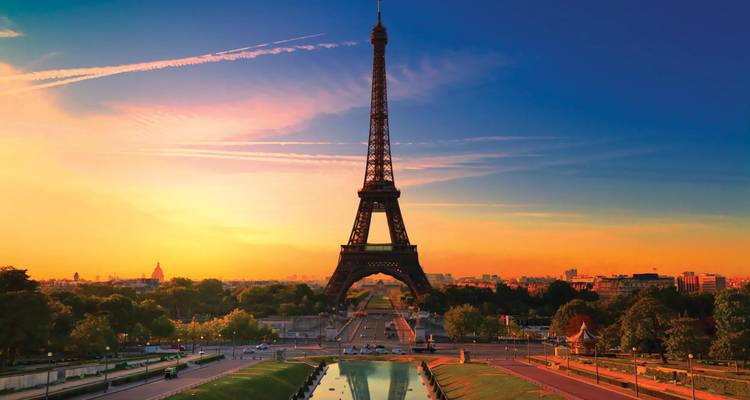 Eiffel Tower rises over Paris at dawn with vibrant orange sky and reflection in fountains.