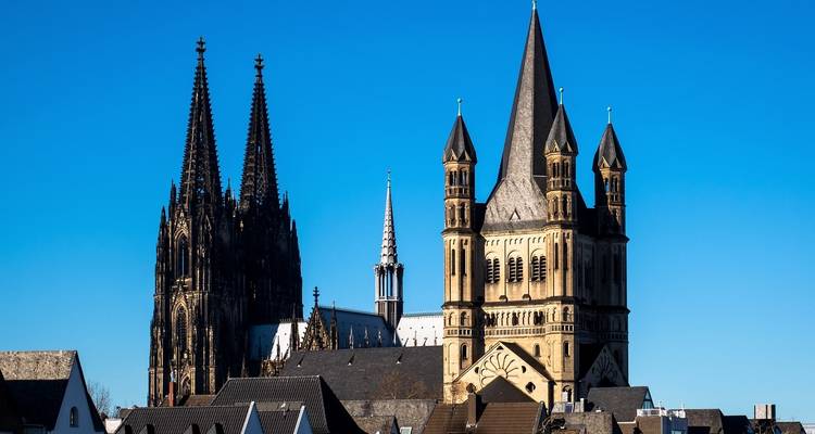 Cologne Cathedral’s twin spires and the Romanesque Great St. Martin Church rise above city rooftops in clear light.