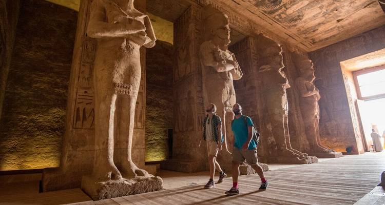 Dos personas explorando un templo con estatuas de piedra masivas.