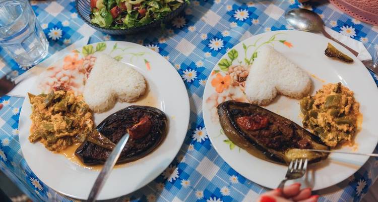 Primer plano de dos platos con arroz en forma de corazón, berenjena rellena y verduras sobre un mantel estampado, listos para disfrutar.