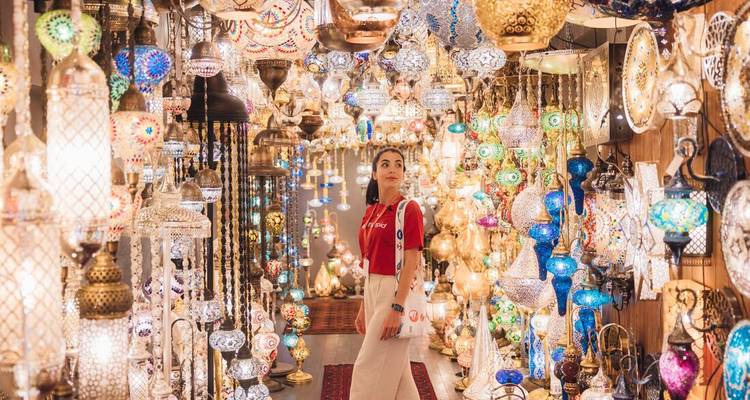 Un visitante admira hileras de lámparas de cristal ornamentadas y coloridas que cuelgan densamente dentro de un puesto de bazar bullicioso.