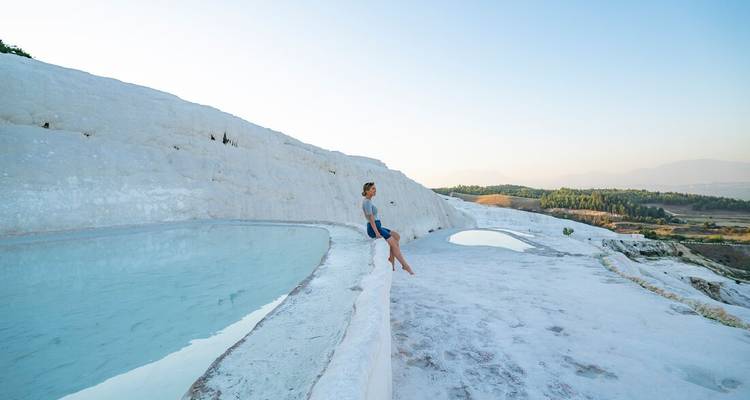 Une femme assise au bord d'un bassin serein parmi les impressionnantes terrasses de travertin blanc de Pamukkale.