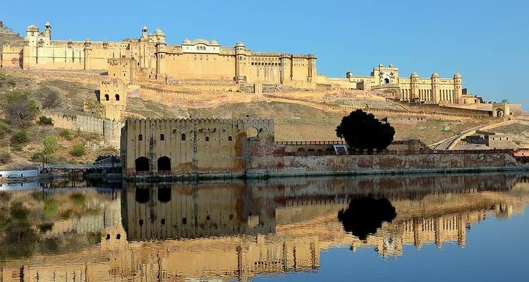 Imposing historic fort with reflection in a lake, clear blue sky.