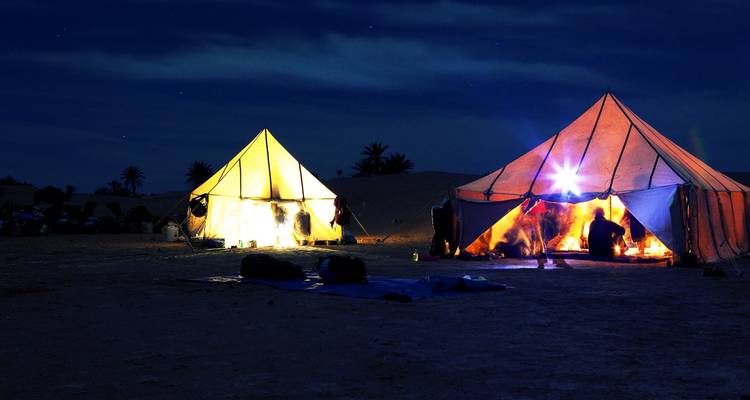 Bunt beleuchtete Zelte, die unter einem sternenklaren Nachthimmel aufgestellt sind.