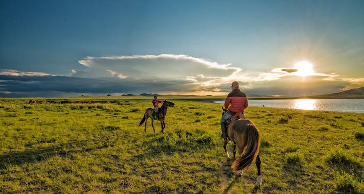 Des gens à cheval près d'un lac au coucher du soleil.