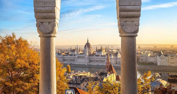 Vista bañada por el sol del Parlamento de Budapest al otro lado del Danube enmarcada por columnas de piedra.