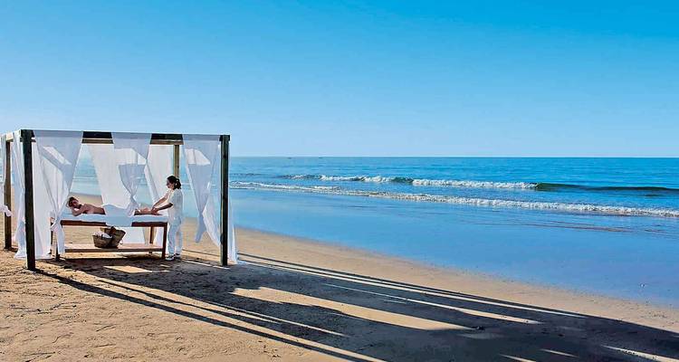 A beach with a massage bed and two people relaxing by the sea.