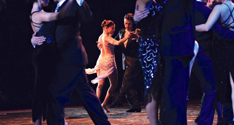 A couple elegantly dancing tango on stage surrounded by onlookers.