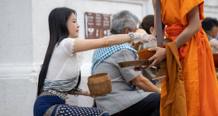 Woman offering alms to a monk on a street.