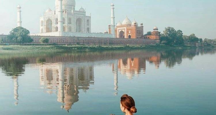 Reflection of the Taj Mahal in the water at sunrise with a person admiring the view.