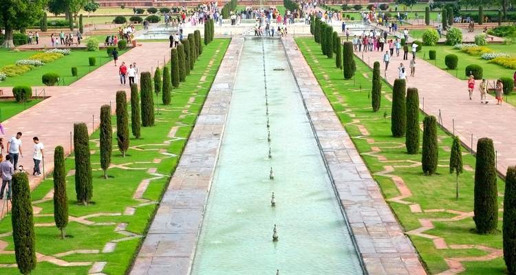 Avenue of trees and fountains leading to the Taj Mahal under a sunny sky.