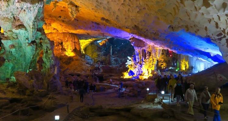 Intérieur d'une grotte éclairé de façon colorée avec des touristes qui marchent.