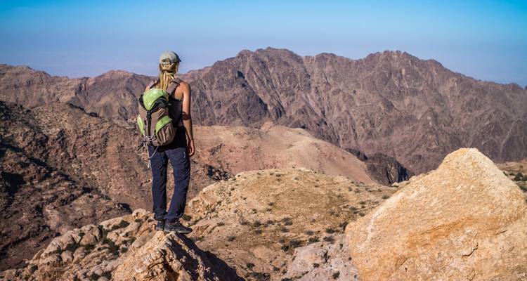 A hiker standing on a rock overlooking a rugged mountainous landscape.