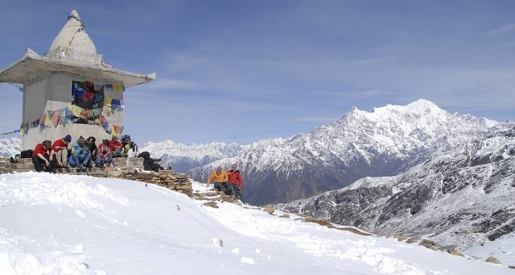 Group of people resting by a snow-covered chapel and mountain view.