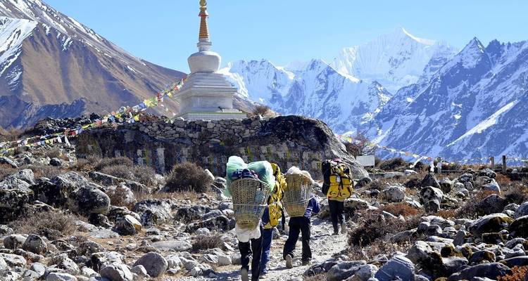 Hikers on a trail with a stupa and snow-covered peaks.