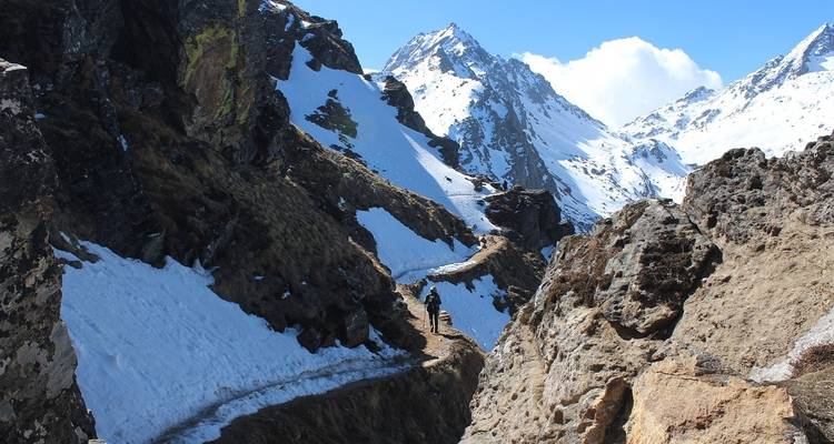 Hiker on a snowy mountain trail surrounded by steep slopes.
