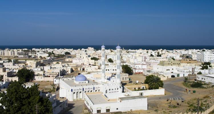 Kustpanorama van Sur's witgekalkte gebouwen die zich uitstrekken naar de Arabische Zee onder een blauwe hemel.
