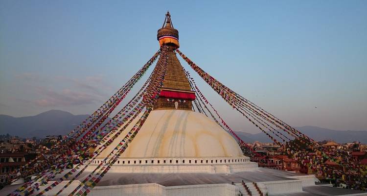 Le Boudhanath Stupa brille à l'heure dorée, drapé de drapeaux de prière colorés contre un ciel aux tons pastel.