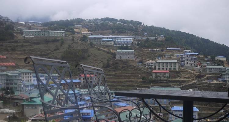 Wolkbedekte heuvels stadje Namche Bazaar gezien vanaf een balkon met lege stoelen