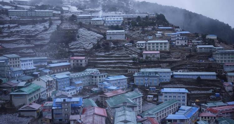Heuvelachtige stad bedekt met lichte sneeuw onder een bewolkte hemel.