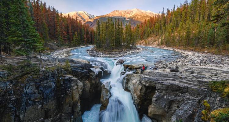 Indrukwekkende waterval die in een canyon stort met besneeuwde Rocky Mountains die gloeien in het avondlicht.