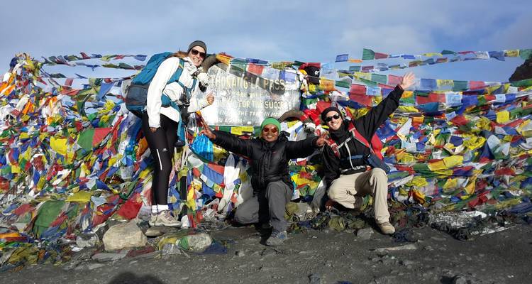 Drie wandelaars bij een bergpas met kleurrijke gebedsvlaggen.