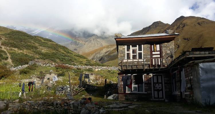 Rustiek huis in een berglandschap met een regenboog.