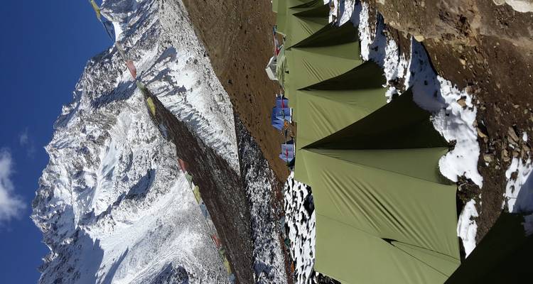 Kampeertenten en gebedsvlaggen in een besneeuwde bergomgeving.