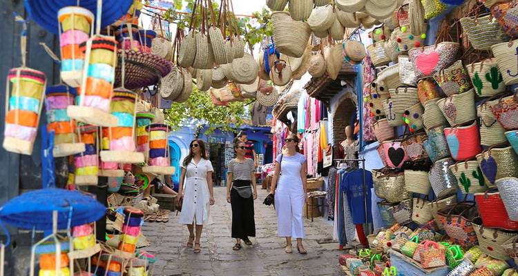 Tres mujeres comprando en un mercado con productos tejidos coloridos.
