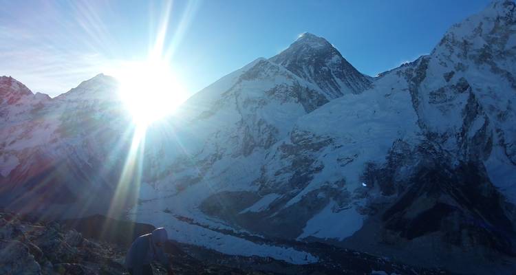 Mountains with sun rays and a person at the bottom.