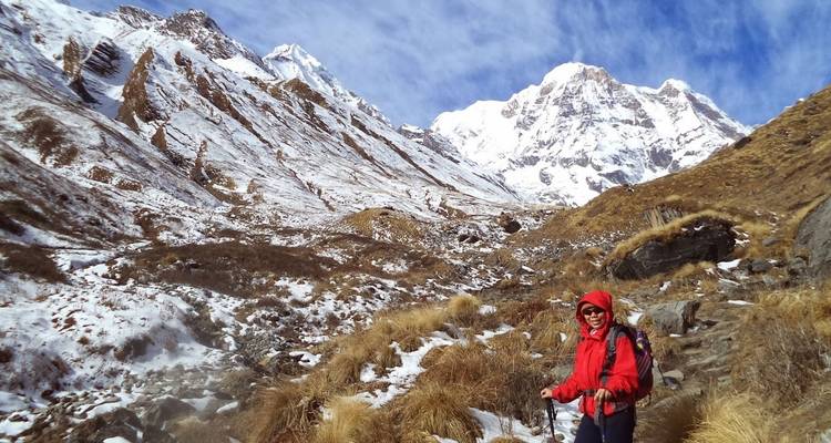 Hiker along a rocky path with snow-covered peaks.