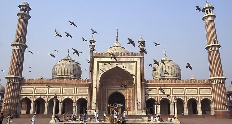 Grand mosque with symmetrical architecture and pigeons flying.