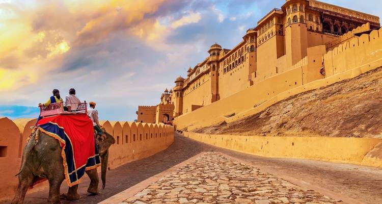 Elephant with tourists near a majestic fort.