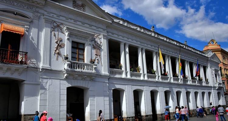 Historic building with multiple flags and people in the foreground